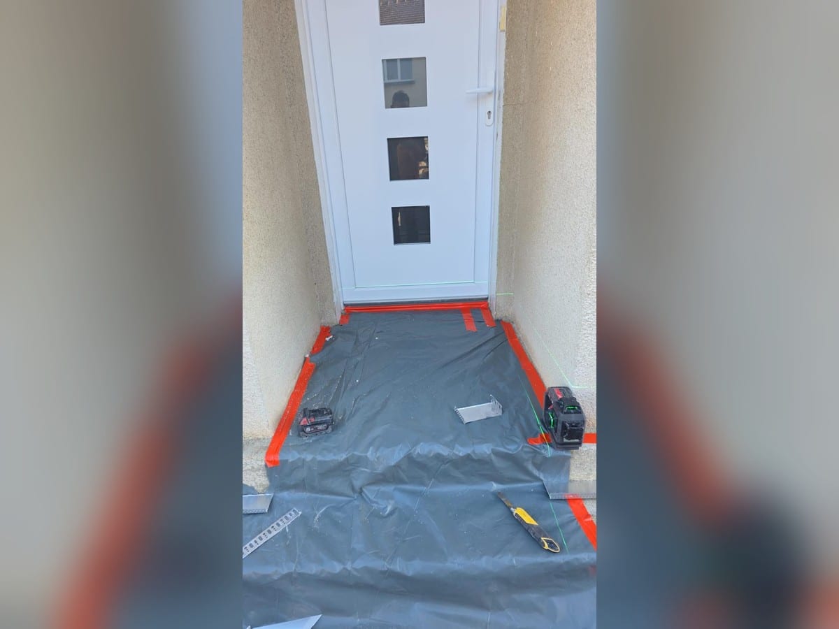 Nivellement au laser d'un seuil de porte en rénovation Laser de nivellement vert sur un seuil de porte protégé par une bâche grise et de l'adhésif rouge pour travaux.