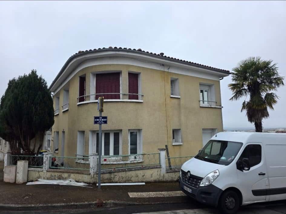Maison jaune à façade arrondie rue Alfred de Musset avec volets marron, palmier et camionnette blanche.